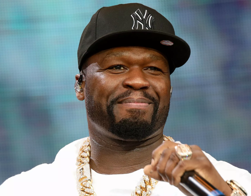 50 Cent performs on-stage in a white t-shirt and baseball cap